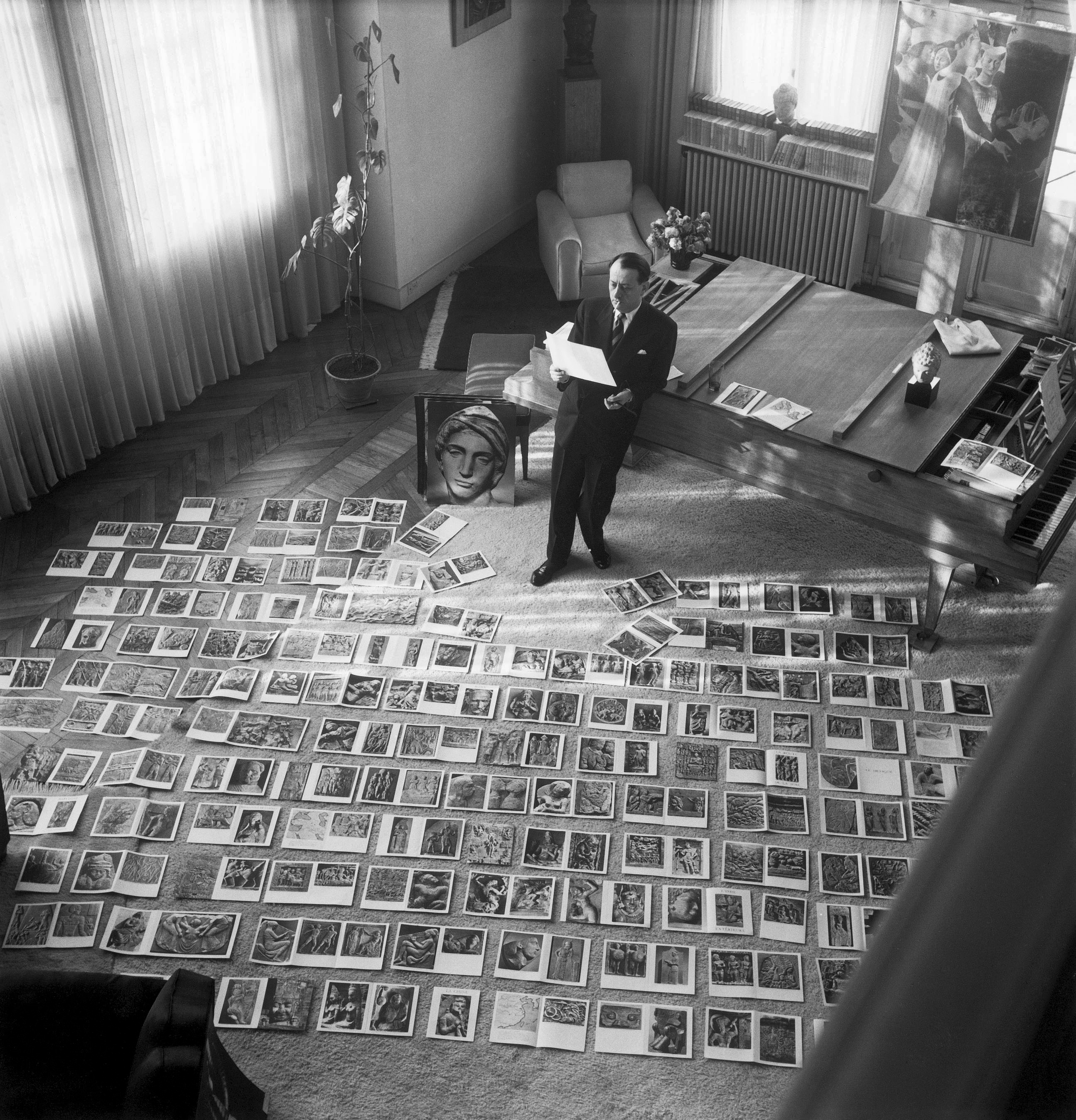 André Malraux nel suo studio, mentre confronta e osserva diverse opere d’arte