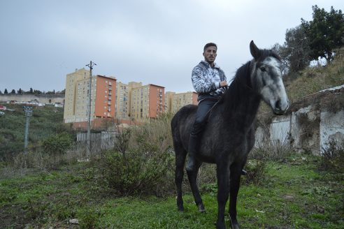 A man on a horse standing in front of apartment blocks in Lisbon's periphery