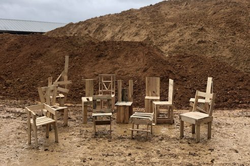 A series of wooden chairs by Material Cultures are stood outside with a bank of soil behind them
