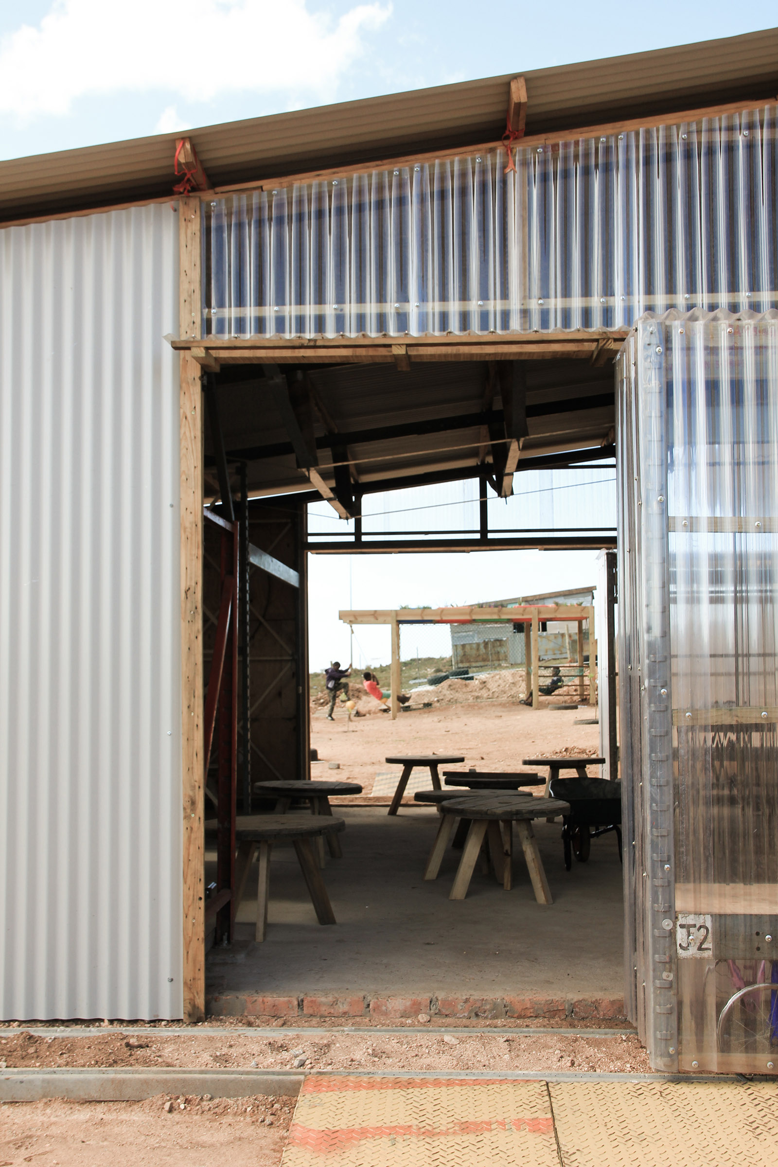 The entrance to the preschool has corrugated cladding, both opaque and transparent, set over a timber frame