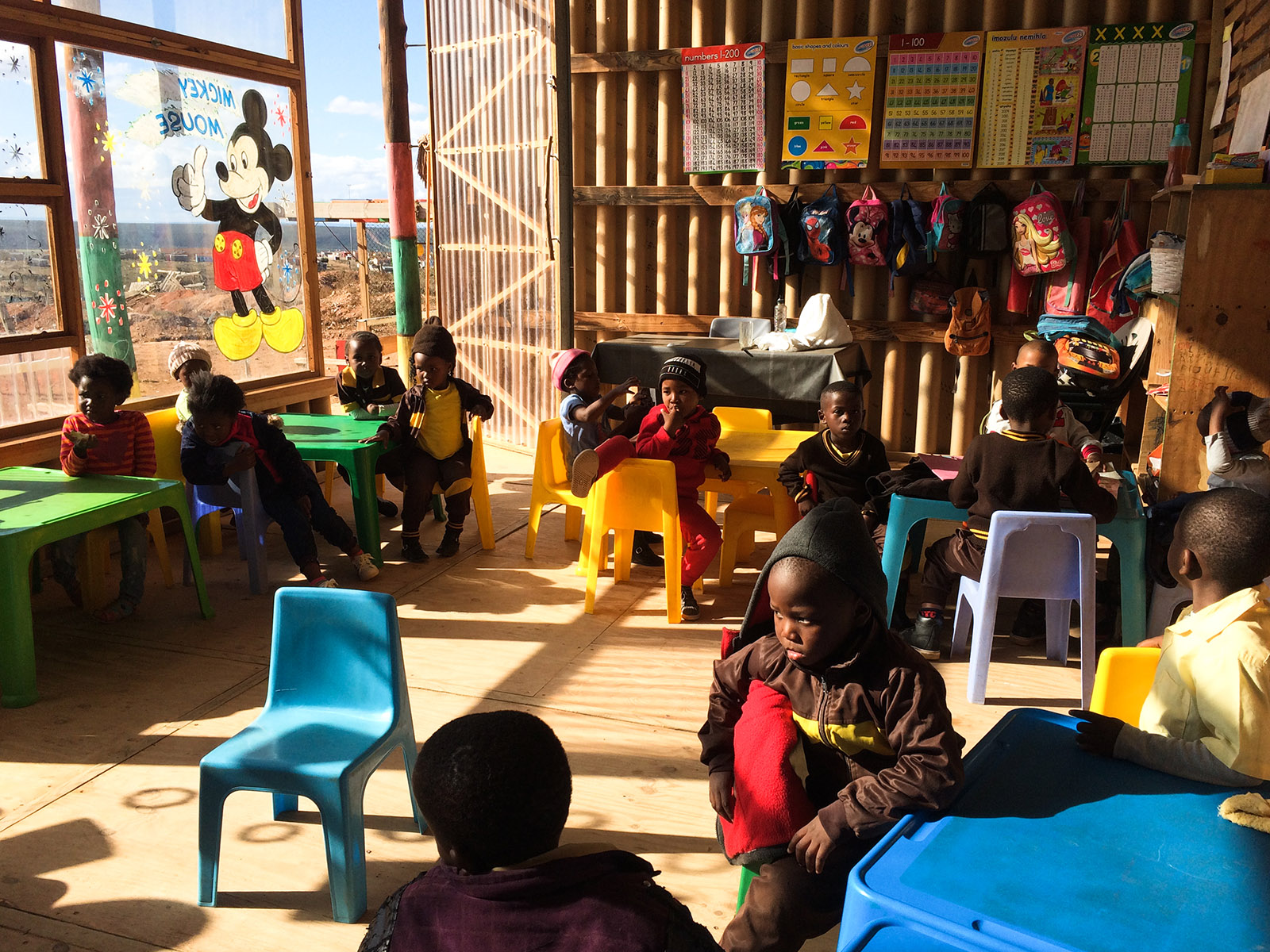 Children sit around on colourful plastic chairs inside the preschool by Collectif Saga