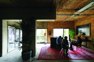 Inside the Farsh Film Studio, concrete meets brick masonry in an apparent straight line – a few people sit around a communal living area with chairs and carpet