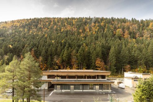 A forest surrounds a tall single-storey building with a flat timber roof