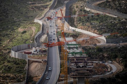 A drone view high over a road under construction with tall fences on either side