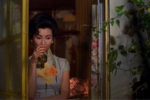 A woman can be seen through the window of her apartment, drinking from a glass