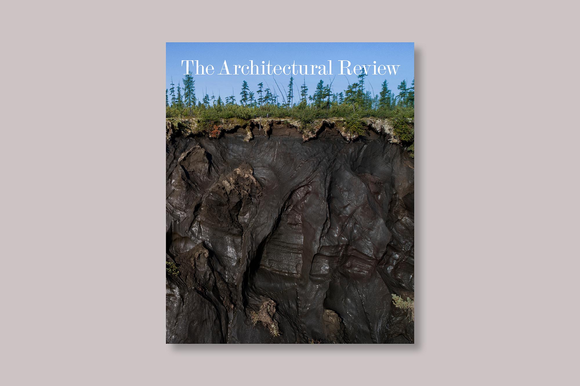 The Architectural Review Ground issue cover, September 2024, depicts a crater in Siberia formed from the collapse of melting permafrost. The photograph is by Katie Orlinsky and features a blue sky in the top 20%, then trees, grass and dark brown mud in gooey forms in the bottom two thirds of the image