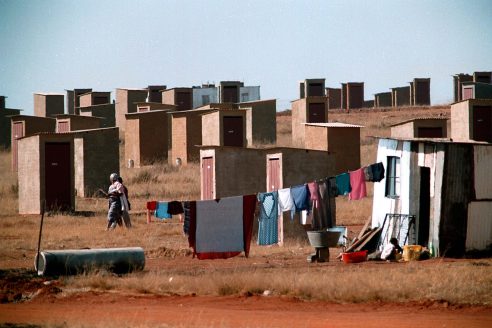 IPMG0344 South Africa, Kagiso, 1995: Women walk through an area marked by toilets and a shack in a new basic housing development by the government near Kagiso township west of Johannesburg, South Africa, 1995. The South African government's housing policy and subsidies made it possible for them to get a low-cost housing unit on land they now own title deed to. Photograph by Greg Marinovich/african.pictures