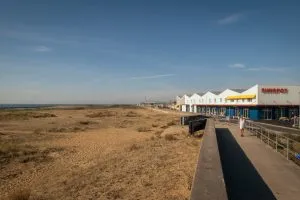 Sunspot by HAT Projects, seen from the sea wall nearby, with beach at left and building at right under a blue sky