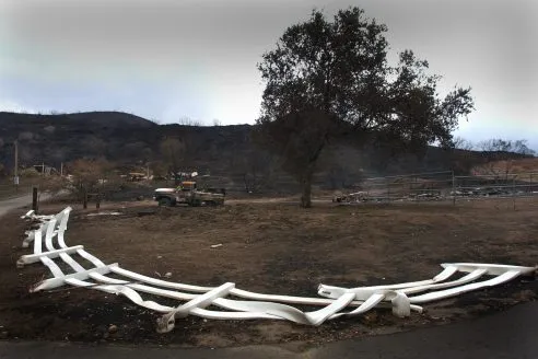 A white vinyl plastic corral fence lies flat on the ground, melted by the intense heat and flames from the Cedar Fire that burned through the Barona Indian Reservation. Several vehicles, and a house were destroyed here just off Barona Rd. (Photo by Don Bartletti/Los Angeles Times via Getty Images)