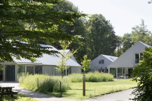 A view of a collection of buildings clad in corrugated metal across a green space and driveway