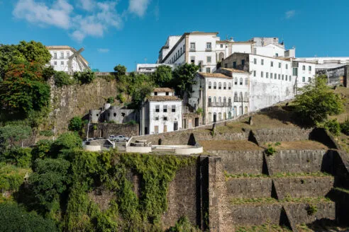 A view of white buildings winding up a stepped cliff covered in green vegetation