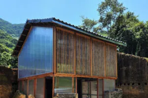 A small-scale building with a pitched roof, wooden frame and polycarbonate walls surrounded by old, crumbling rammed earth walls