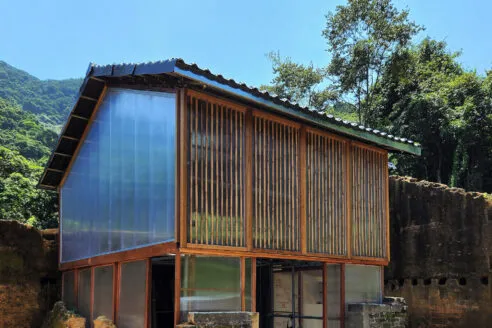 A small-scale building with a pitched roof, wooden frame and polycarbonate walls surrounded by old, crumbling rammed earth walls