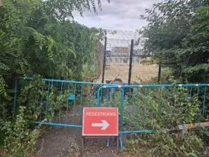 Fencing and a red sign with an arrow pointing to the right and the word "pedestrians". There's more fencing and a path on the background.